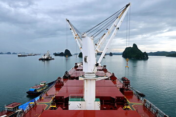Loading bulk cargo of limestone from barges into a bulk carrier by using ship cranes and grabs at...