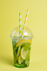 Mojito cocktail in plastic glass with tube on yellow background. ool drink in the summer for...