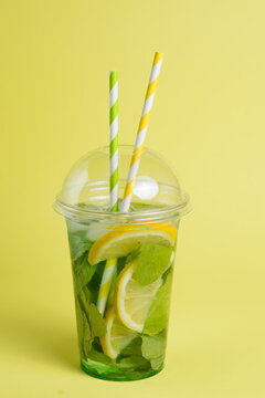 Mojito cocktail in plastic glass with tube on yellow background. ool drink in the summer for takeaway