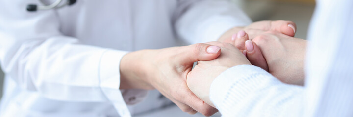 Doctor holding hands of patient in clinic closeup