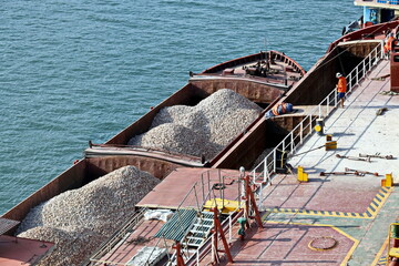 Loading bulk cargo of limestone from barges into a bulk carrier by using ship cranes and grabs at the port of Campha, Vietnam. October,2020. 