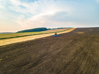 Aerial view of a tractor plowing black agriculture farm field after harvesting in late autumn.