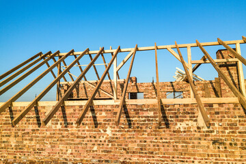 Unfinished brick house with wooden roof structure under construction.