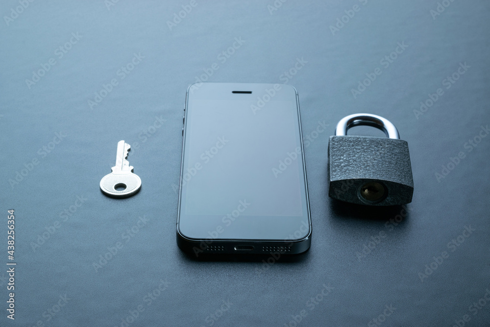 Wall mural Technology security. Modern space grey mobile phone with padlock, key on dark background. Smartphone security breach concept.