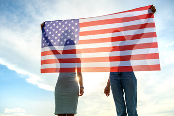 Silhouette of two young friends women holding USA national flag in their hands standing together outdoors. Patriotic girls celebrating United States independence day.