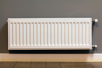 White metal heating radiator mounted on gray wall inside a room.