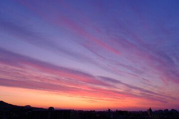  神戸市東灘区の高層マンションからの日の出、東の空がオレンジ色に染まり、神戸・芦屋・西宮の街並みがシルエットで浮かぶ。一日の始まり。
