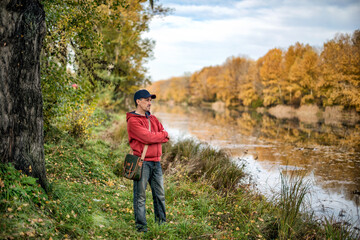 Fototapeta premium A man with a shoulder bag and a cap walking in a park in summer.