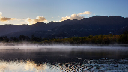 Mist hangs over the lake surface with mountains in the background.