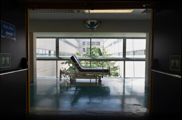 solitary bed in the corridor of a hospital behind the entrance door and with a luminous background