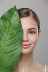 Portrait of woman and green leaf. Organic beauty. Gray background.