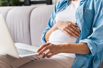 Cropped closeup portrait of a pregnant woman`s belly with laptop searching browsing informantion about fertility and child care, maternity leave. Future mother, motherhood concept - obrazy, fototapety, plakaty