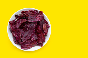 Purple sweet potato chips in white plate on yellow background.