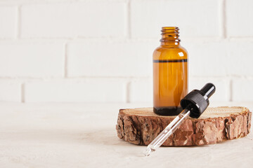 brown glass bottle with a pipette on a saw cut of a tree, a white brick wall on the background