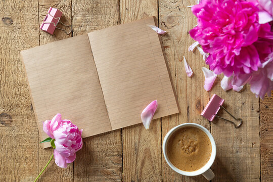 Opened blank notebook vintage, fresh pink peonies and cup of coffee on rough hewn wooden table. Top view, copy space .