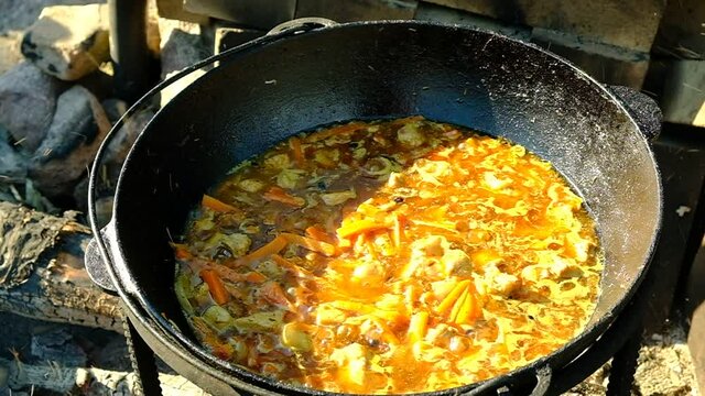 Cooking the Uzbek national dish - pilaf. Cast iron cauldron on a stand. Fire from wood firewood. The basis of plovazirvak. Zirvak from meat. onions, carrots, cumin, turmeric, oil, frying. Grinding wit