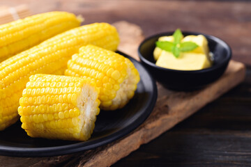 Sweetcorn cob and butter in a bowl on wooden background