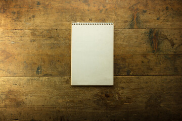 Blank white cover of vertical type notebook, on a grungy or rustic old wooden table.