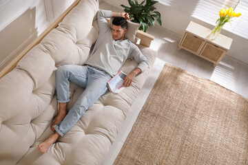 Man with newspaper sleeping on sofa at home, view from above