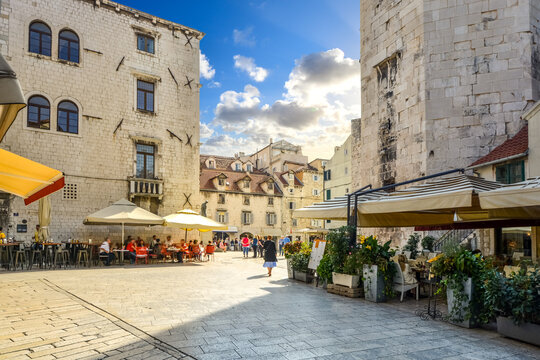 Fototapeta Tourists enjoy a sunny day as they eat at sidewalk cafes and window shop at the Fruit Square, inside the ancient Diocletian's Palace in Split, Croatia