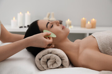 Obraz na płótnie Canvas Young woman receiving facial massage with gua sha tool in beauty salon