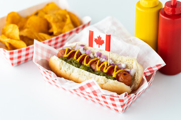 A hotdog with a Canada flag pick served with potato chips and a bottle of ketchup and mustard in...