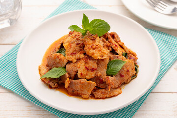 Stir fried pork with Thai chili paste and Thai sweet basil leaves or moo pad nam prik pao, served on the white plate. It is a simple hot sweet Thai food dish that goes well with plain cooked rice.