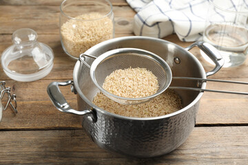 Sieve with rice in pot on wooden table