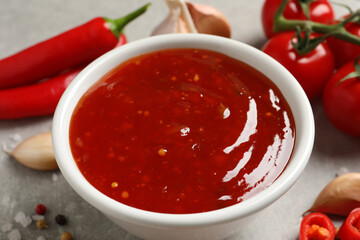 Spicy chili sauce in bowl on grey table, closeup
