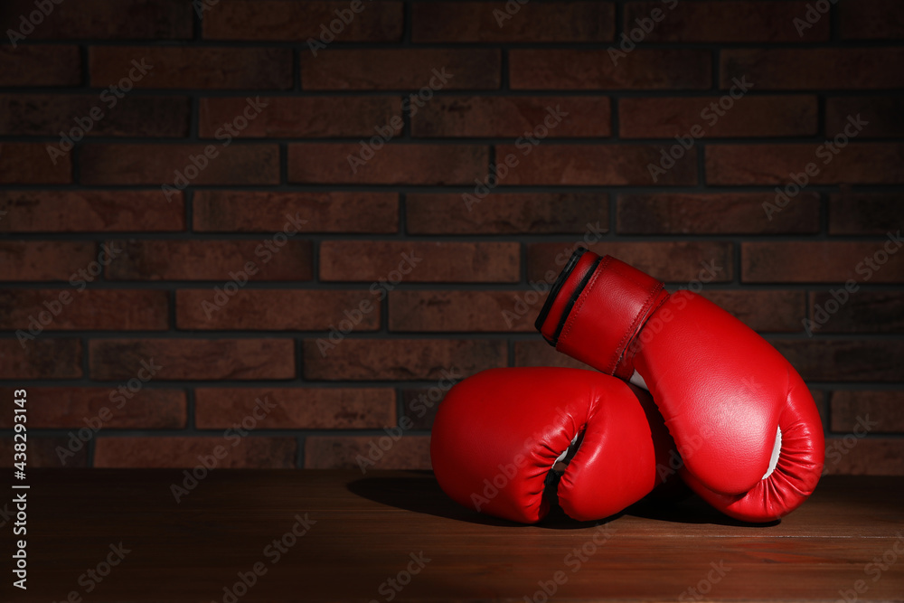 Wall mural pair of red boxing gloves on wooden table near brick wall