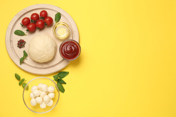 Raw dough and other pizza ingredients on yellow background, flat lay. Space for text