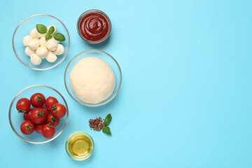 Raw dough and other pizza ingredients on light blue background, flat lay. Space for text