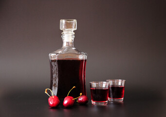 Cherry liqueur in a glass bottle and two glasses, next to ripe berries on a black background.