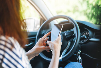 Crop photo of young woman driver using mobile phone in hands sitting in car in the summer time