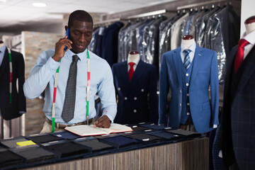 Smiling afro-american man tailor taking order at counter in sewing workshop. High quality photo