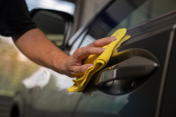 detail of hand wiping door of a car with cloth