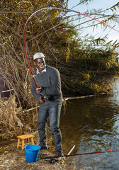 Mature African man standing near river and pulling fish expressing emotions of dedication