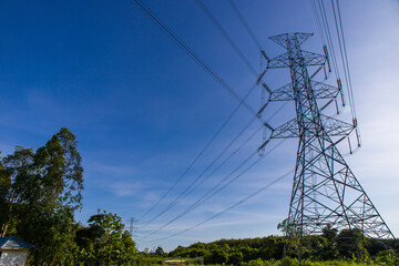 Landscape view of high voltage electric and electrical wires in the verdant meadow on deep blue sky background. High electric power transmission line tower is located in meadow. Thailand.