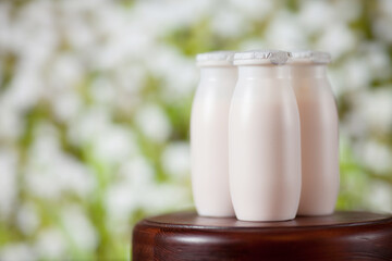 Natural liquid yogurt with probiotics in small plastic bottles on wooden table on background of meadow with flowers.