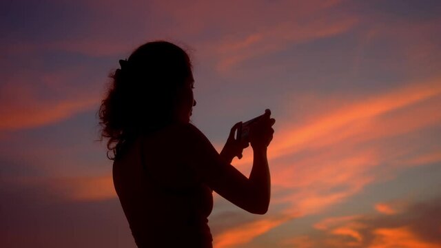 Tourist Woman Taking Photos with Mobile Phone Camera of Amazing Sunset at the coats