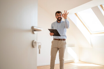 Portrait of handsome real estate agent holding okay gesture sign in new house.