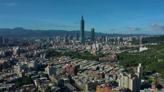 Cinematic aerial view showing skyline of Taipei City with high rising Tower 101 and mountains in background.