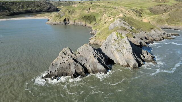 Rocky Cliffs At Three Cliffs Bay Beach By The Calm Ocean In Swansea, Wales, United Kingdom. - aerial