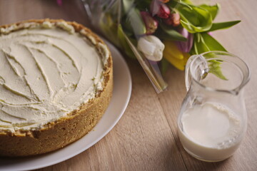 Fototapeta na wymiar Banana homemade cake, a congratulatory bouquet of flowers and a jug of milk on the table.