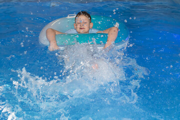 A Beautiful happy boy swims in the pool with a circle