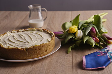 A cake, greeting flowers, a jug of milk, and a woman's silk scarf are laid out on a wooden table.