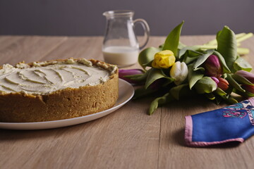 A cake, greeting flowers, a jug of milk, and a woman's silk scarf are laid out on a wooden table.
