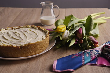 Fototapeta na wymiar A cake, greeting flowers, a jug of milk, and a woman's silk scarf are laid out on a wooden table.