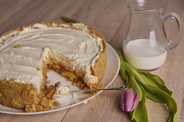 A piece of cake, a jug of milk, and a tulip are spread out on the table.