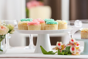Dessert stand with tasty cupcakes and flowers on table